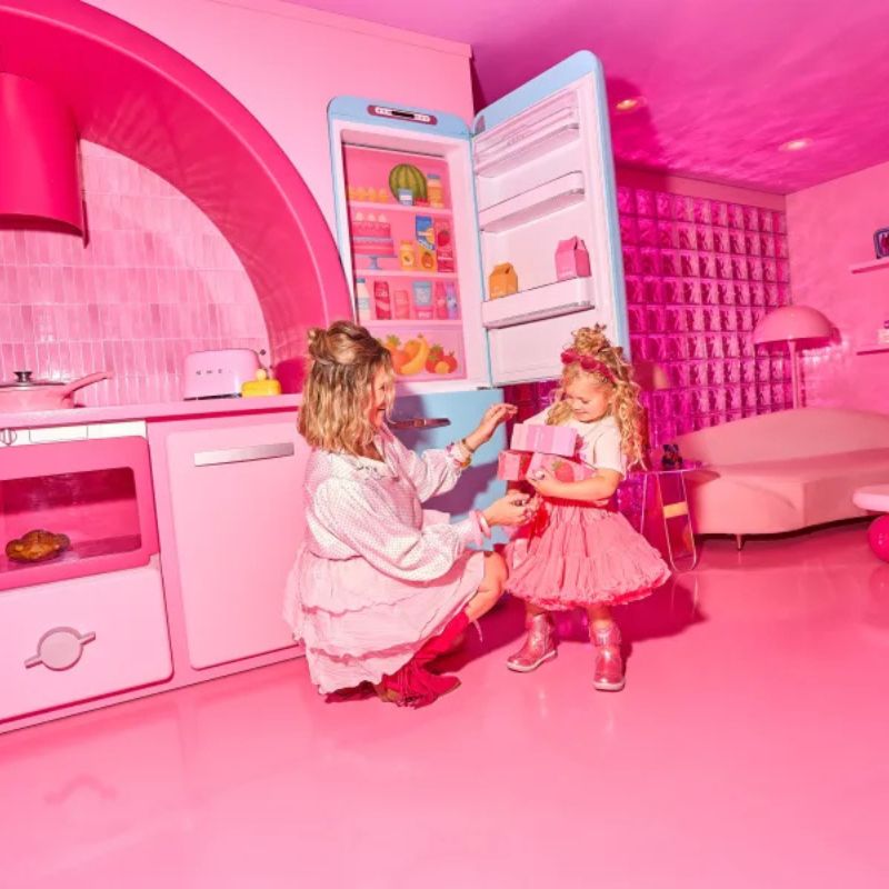 Mother and daughter exploring a life-sized pink Barbie kitchen