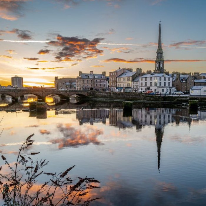 Ayr's riverside buildings and bridge reflected in the water beneath a colourful sky
