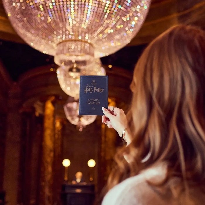 A visitor holding an Activity Passport beneath the Gringotts chandeliers