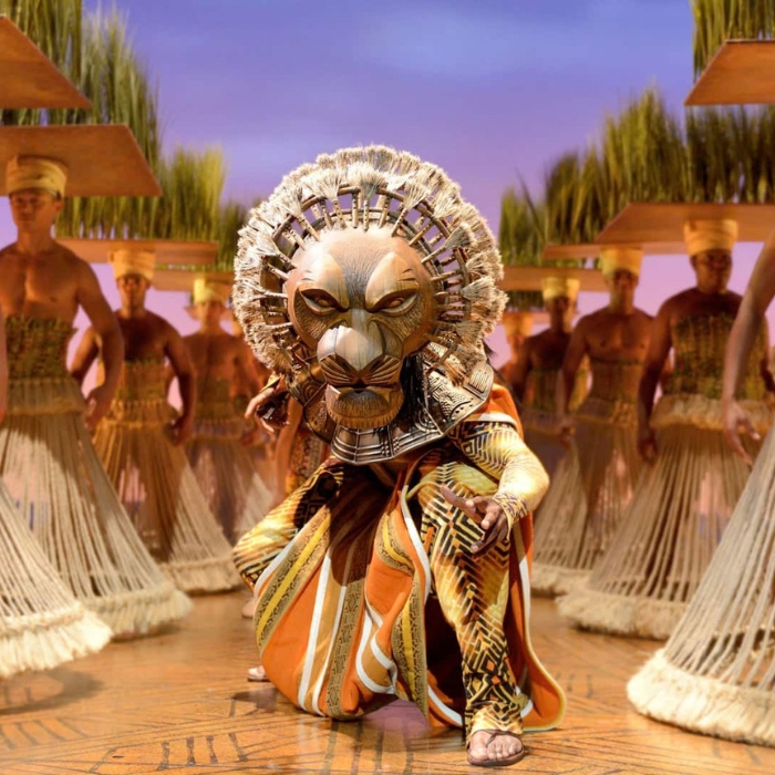 A lion character and ensemble performers on stage in Disney’s The Lion King