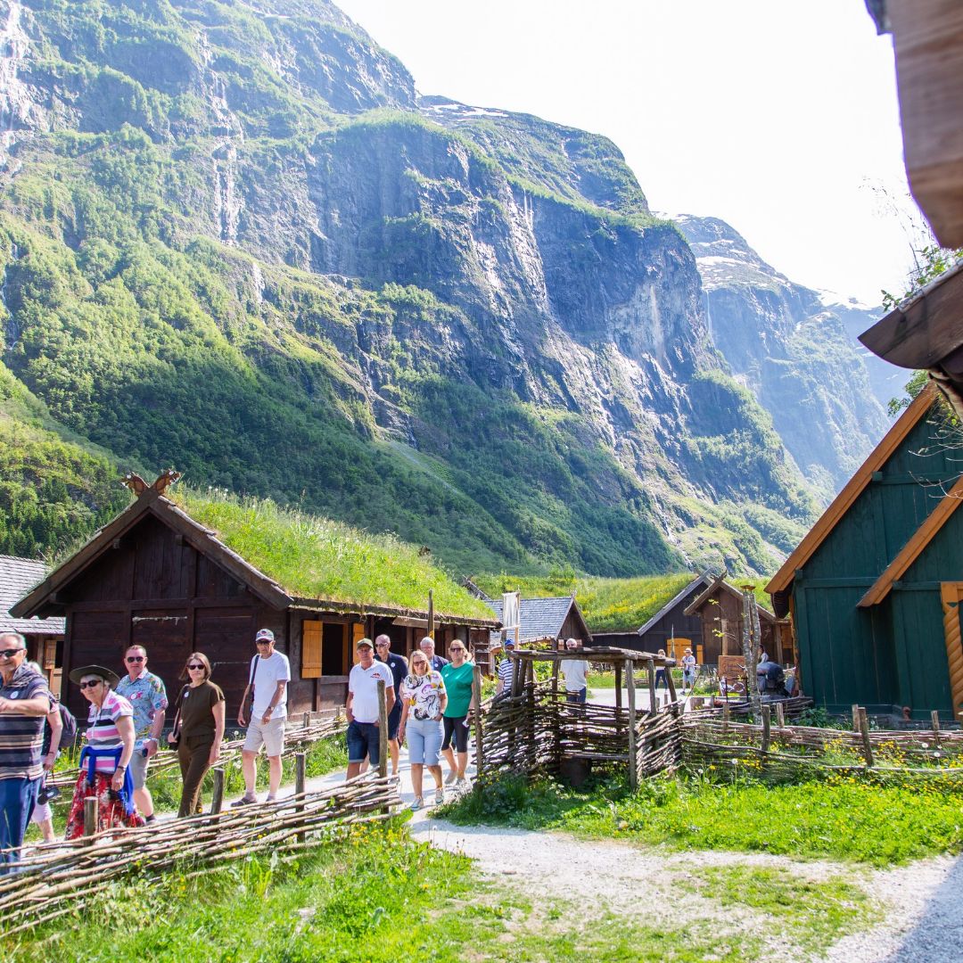 Visitors exploring traditional buildings beneath the mountains in Fl&aring;m