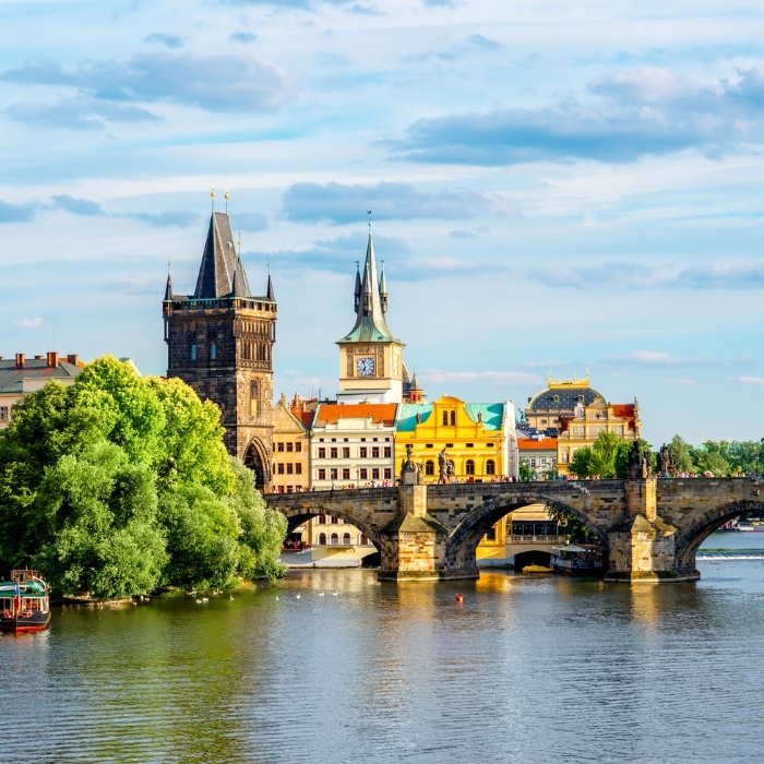 Historic towers and green riverbanks beside a bridge in Prague
